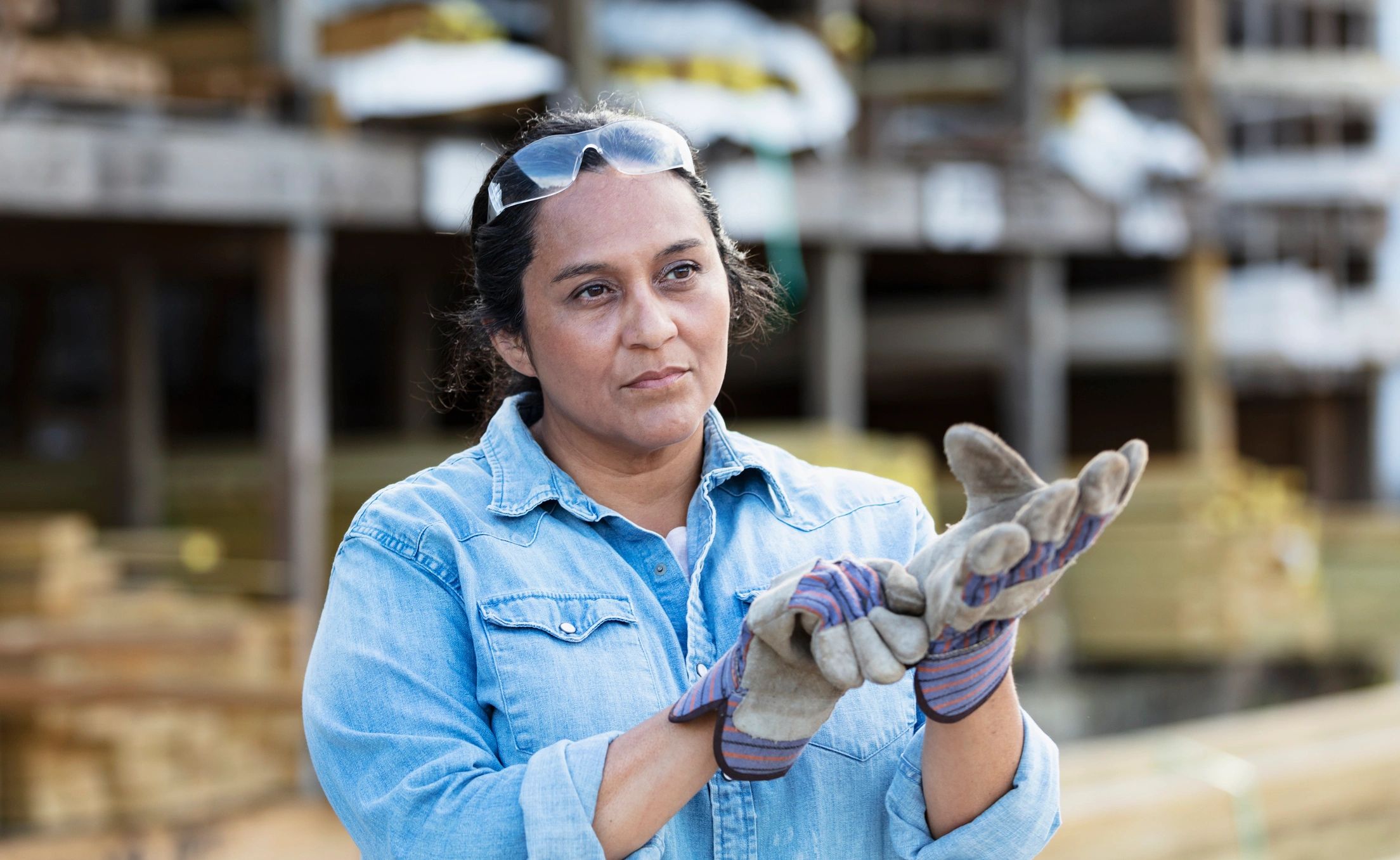 Worker putting on gloves in a lumberyard setting