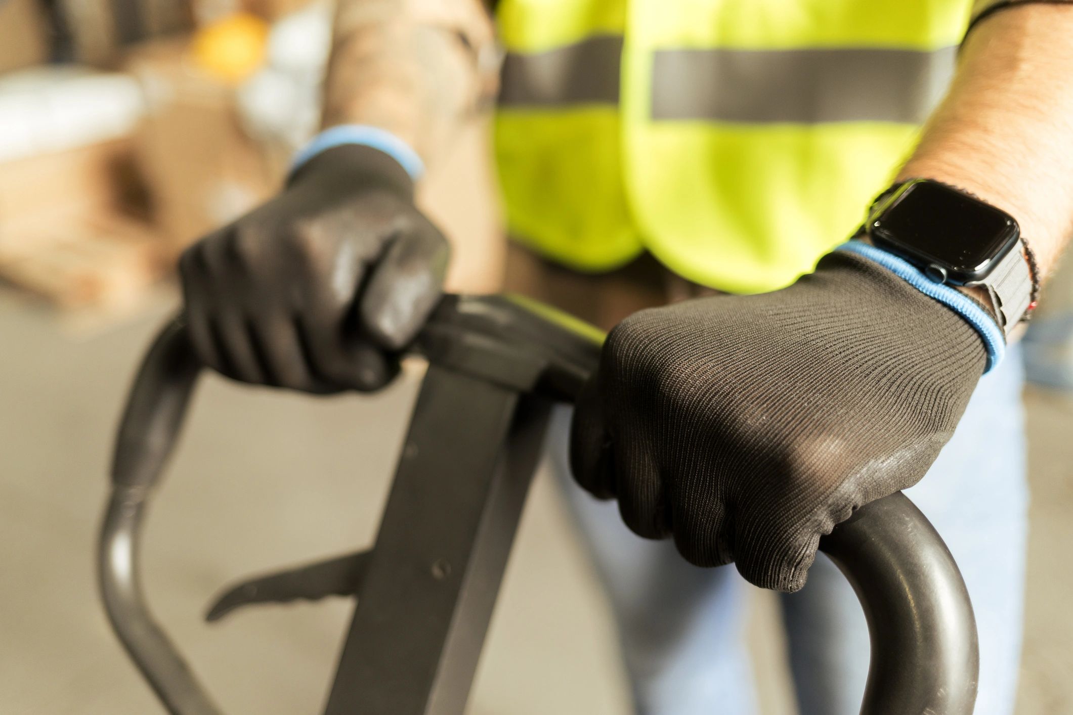 Close-up of gloved hands operating a pallet jack handle in a warehouse